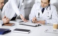 Group of unknown doctors are sitting at the desk and discussing medical treatment, using a clipboard, close-up. Team of