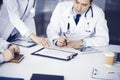 Group of unknown doctors are sitting at the desk and discussing medical treatment, using a clipboard, close-up. Team of