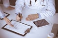 Group of unknown doctors are sitting at the desk and discussing medical treatment, using a clipboard, close-up. Team of