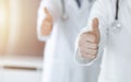 Group of unknown doctors standing as a team with thumbs up or Ok sign in hospital office, close-up. Medical help