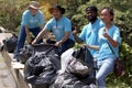 Group of volunteers in blue t-shirt holding garbage bag at rubbish dump, ecology people cleaning and picking up trash to reduce Royalty Free Stock Photo