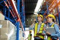 Group of warehouse workers with hardhats and reflective jackets using tablet, walkie talkie radio and cardboard while controlling