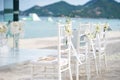 A group of white chiavari chairs on the beach wedding preparation, cones of roses petals - back side view