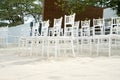 A group of white chiavari chairs on the beach wedding preparation, cones of roses petals - front side, low angle view