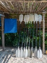 Group of white kayak paddles drying rests on a wooden storage under the roof on the sandy beach.