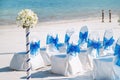 A group of white spandex chairs cover with blue organza sash for beach wedding venue setup