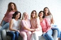 Group of women with silk ribbons sitting on sofa against brick wall.