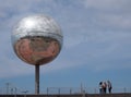 A group of women stood near the giant glitter ball on blackpool promenade with blue sky and reflection of the town in the mirrored