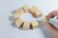 Group of wooden cubes together building a circle, hand adds the missing one, symbol of teamwork, solidarity and cohesion, light