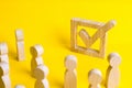 A group of wooden figures of people surround and look at a tick in the box. Voters take part in elections. Voting, referendum, soc