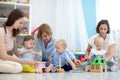 Group of workers with babies in nursery or kindergarten. Moms playing with kids in creche Royalty Free Stock Photo