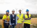Group of workers and industrial engineers looking at the camera in a field of windmills