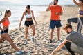 Group of young adults doing exercises on sandy beach. beardy guy drinking water from a plastic bottle Royalty Free Stock Photo