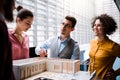 Group of young architects with model of a house standing in office, talking.