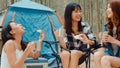 Group of young asia camper friends sitting in chairs by tent in forest. Teenager girl traveler relax and talk on a summer day at Royalty Free Stock Photo