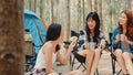 Group of young asia camper friends sitting in chairs by tent in forest. Teenager girl traveler relax and talk on a summer day at Royalty Free Stock Photo