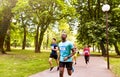 Group of young athletes running in green sunny park.