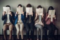 Group of young business people covering their faces with papers while waiting for job interview, Young people hiding their faces