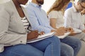 Group of young business people sitting on chairs in a row and writing in notebooks.