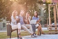 Group of young caucasian businesspeople laughing at bench in a park with their cell phones, laptop, tablet. Looking at camera, eye Royalty Free Stock Photo