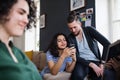 A group of young friends with smartphone sitting on sofa indoors, house sharing concept.