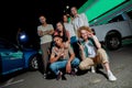 A group of young cool-looking friends of different nationalities sitting and standing and posing together outside on a