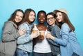 Group of young five female friends of different nationalities holding a cups of coffee to go over blue background. Royalty Free Stock Photo