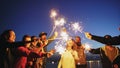 Group of young friends having a beach party. Friends dancing and celebrating with sparklers in twilight sunset Royalty Free Stock Photo