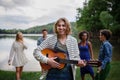 A group of young friends having fun near a lake, laughing and playing guitar. Royalty Free Stock Photo