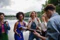 A group of young friends having fun near a lake, laughing and playing guitar. Royalty Free Stock Photo