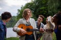 A group of young friends having fun near a lake, laughing and playing guitar. Royalty Free Stock Photo