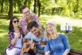 Group of young friends playing guitar and taking a selfie on a park bench Royalty Free Stock Photo