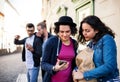 A group of young friends with smartphone standing outdoor in town, talking.