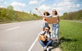 Group of young friends thumbing their ride on road with empty sign, playing guitar, having autostop journey, free space Royalty Free Stock Photo