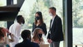 Group of young happy business people talk standing near large office window wearing COVID-19 face masks protection. Royalty Free Stock Photo