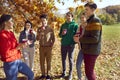 Group of a young happy smiling friends drinking coffee or tea in the autumn park. Royalty Free Stock Photo