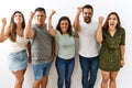 Group of young hispanic friends standing together over isolated background angry and mad raising fist frustrated and furious while Royalty Free Stock Photo