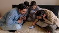 Group of young Indian males and females looking at a mobile phone while sitting on a bed