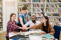 Group of young joyful multiracial college students collaborating on project, sitting at the table in library and putting Royalty Free Stock Photo