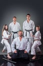 Group of young karate players posing with their coach on the gray background