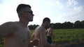 Group of young men running along rural road over field with sun flare at background. Profile of male athletes jogging in