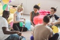 group of young multicultural friends in party hats sitting on floor with balloons in decorated