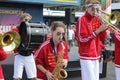 Group of young musicians in red and white uniforms playing their instruments outdoors.