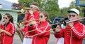 Group of young musicians in red and white uniforms playing their instruments outdoors.