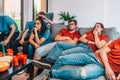 group of young people, bored, watching a football match on tv. tired youngster friends, at a house party. leisure