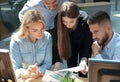 Group of young people in casual wear sitting at the office desk and discussing something while looking at PC together.