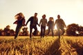 A group of young people running through the grass in the park at sunset. Royalty Free Stock Photo