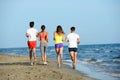 Group of young people running in the sand on the shore of a beach by the sea at sunset during a sunny summer holiday vacation Royalty Free Stock Photo