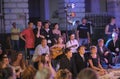 Group of young people sitting on karemats outdoor watching the play of the street theatre actors, girl playing guitar in