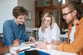 Group of young people sitting at the table and working together in office. Pretty girl and two boys happily discussing Royalty Free Stock Photo